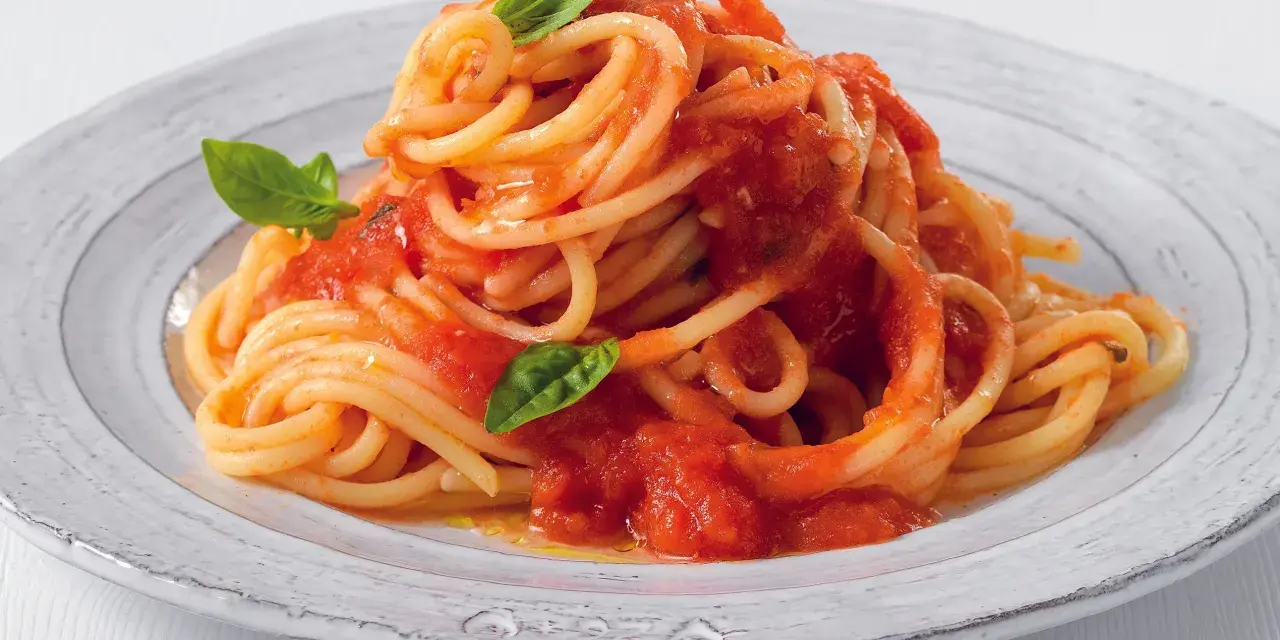 Un piatto di pasta fatta in casa, spaghetti al pomodoro fresco e basilico, serviti su un piatto rustico.