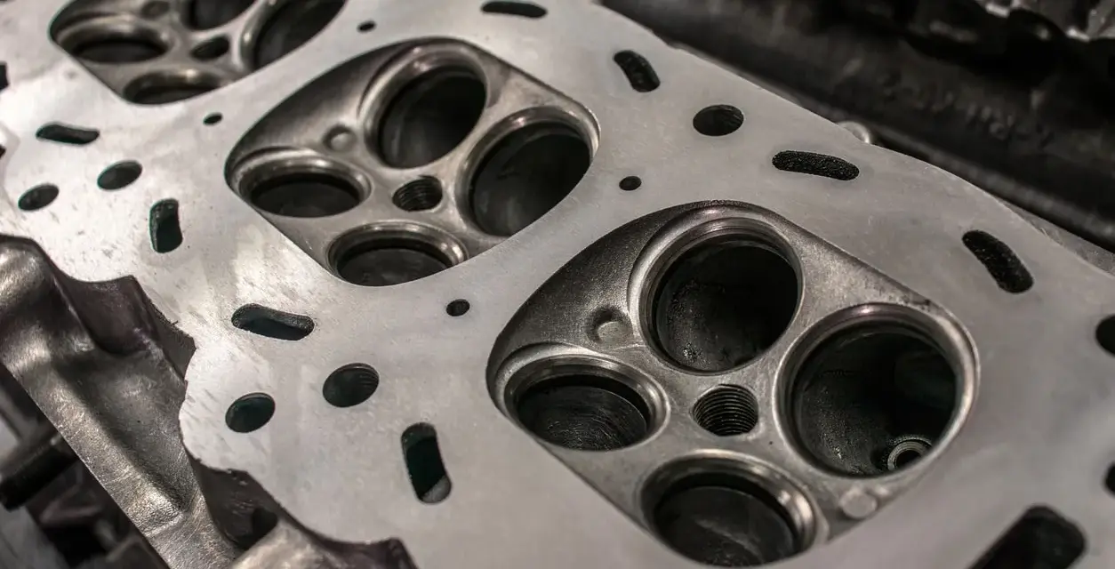 Nahaufnahme eines Zylinderkopfs eines Autos. Die Ventilsitze und die Bohrungen für die Zündkerzen sind sichtbar. Eine neue Kopfdichtung für das Auto wird bald montiert.