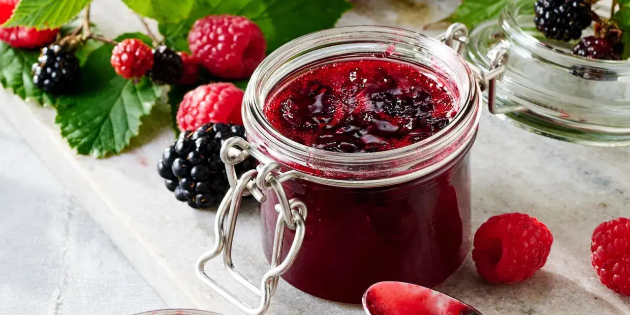 Frische Brombeeren und Himbeeren neben einem Glas selbstgemachter Marmelade. Perfekt für brombeeren rezepte schnell und einfach.