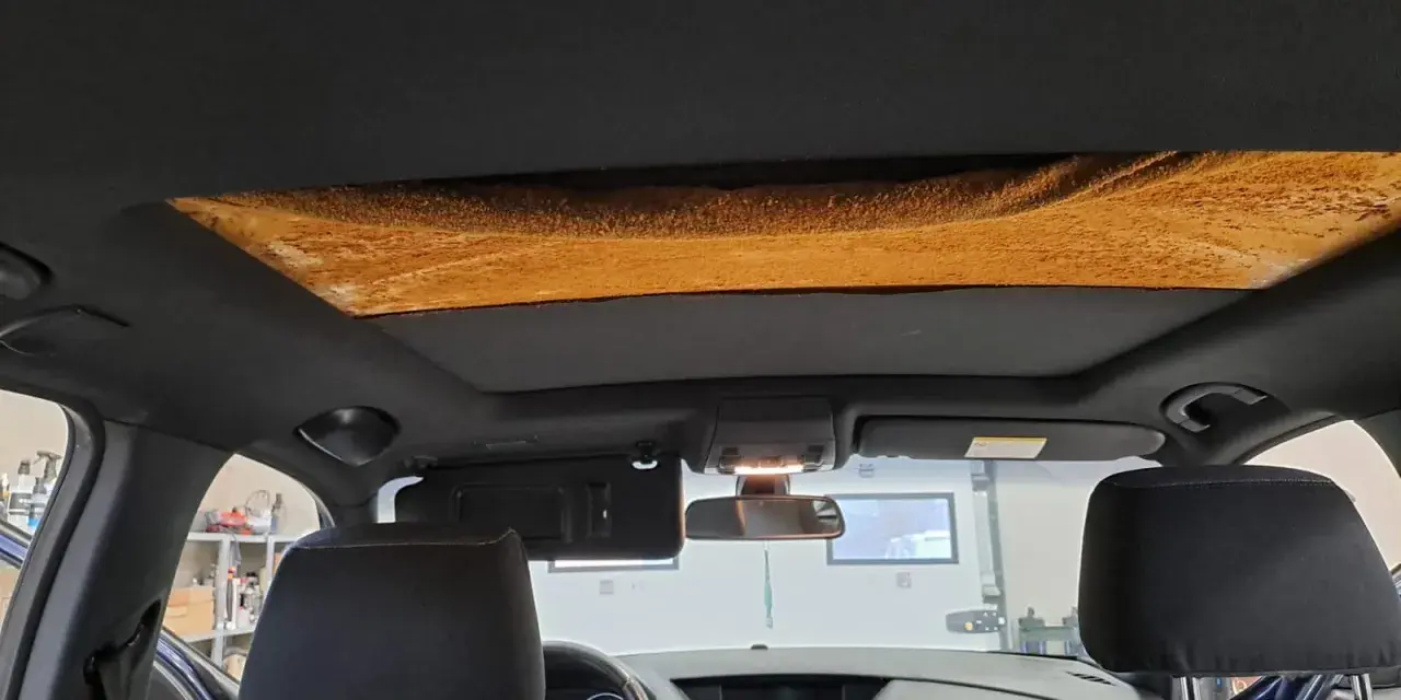 Widok wnętrza samochodu z widoczną, zniszczoną podsufitką, która wymaga oklejania.