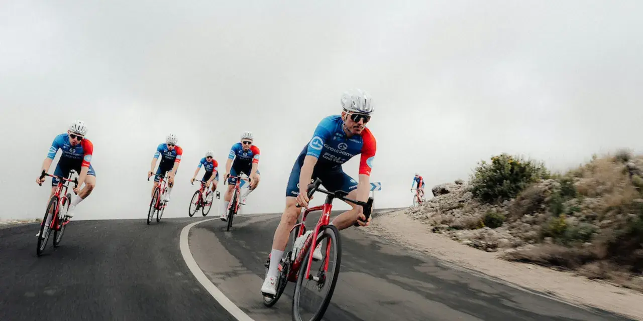Cyclists in blue and red kits race downhill, showcasing the intense effort behind the Tour de France average speed.