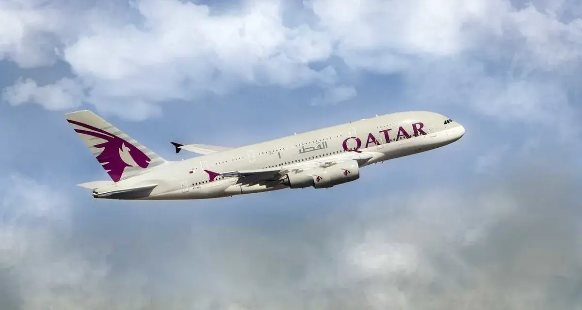 Qatar Airways Airbus A380 airplane in flight against a cloudy blue sky.