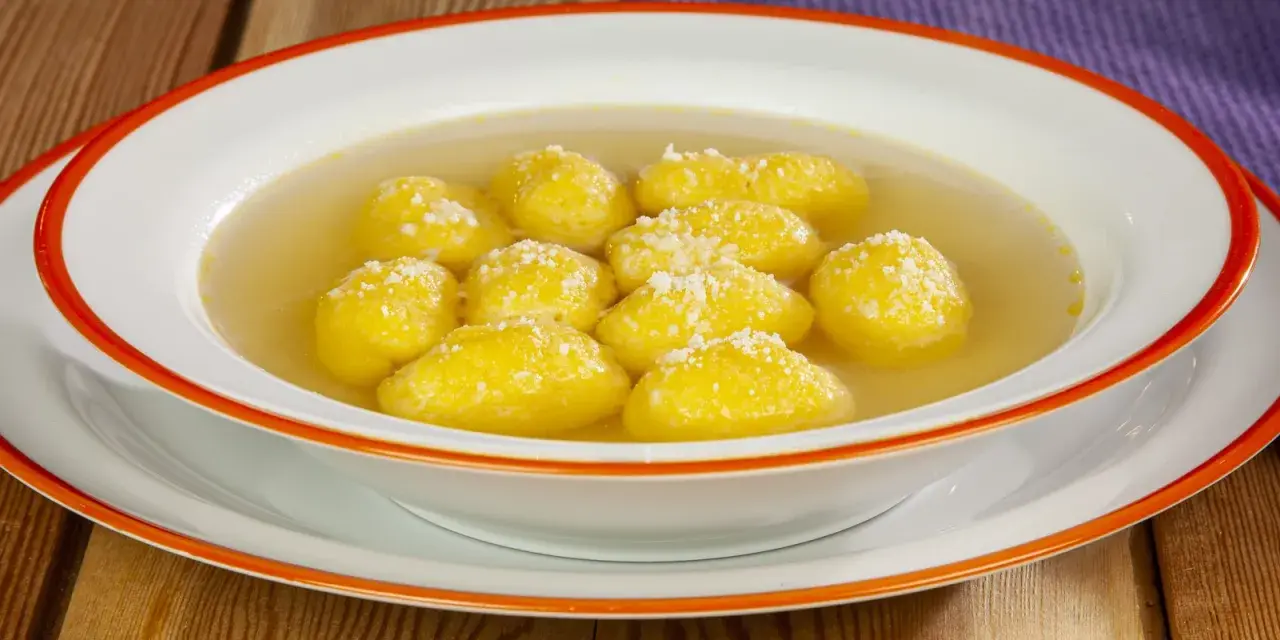 Una ciotola di semolino dosi per 1 persona, con palline dorate in brodo, cosparse di formaggio grattugiato.