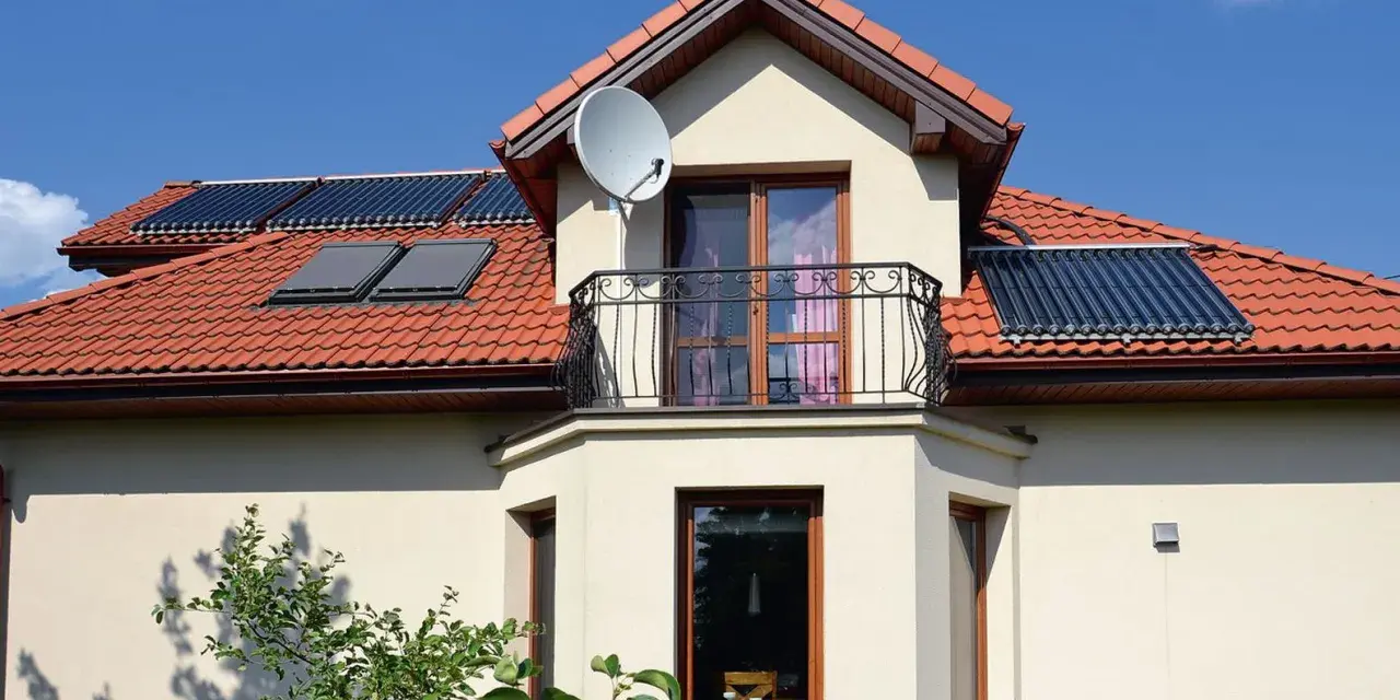 Elegancki wykusz w domu z balkonem i anteną satelitarną. Na dachu widoczne kolektory słoneczne.