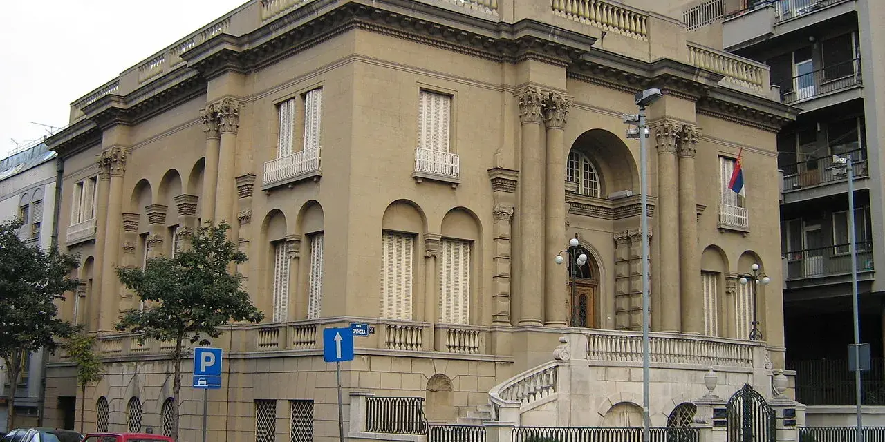 Elegancki budynek, Muzeum Tesli, z kolumnami i łukami. Przed nim schody i ogrodzenie.
