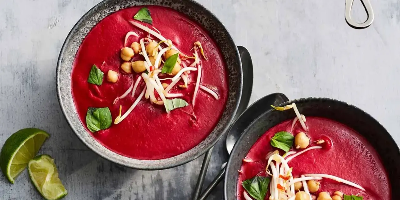 Zwei Schalen cremiger, **roter Bete Suppe mit Kokosmilch und Orangensaft**, garniert mit Kichererbsen und Sprossen.