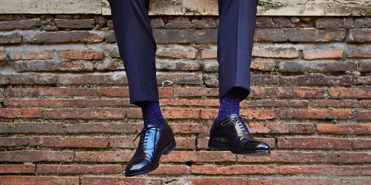 Uomo con calzini blu a pois bianchi e scarpe nere lucide. Un perfetto abbinamento calzini scarpe uomo per un look elegante.
