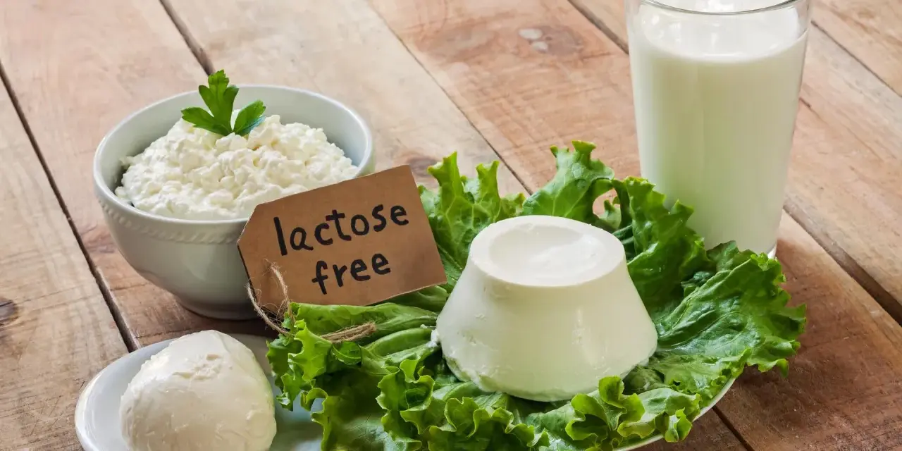 Serek wiejski, kulka mozzarelli i ser w kształcie stożka na sałacie, obok szklanki mleka. Etykieta głosi "lactose free", co oznacza brak laktozy.