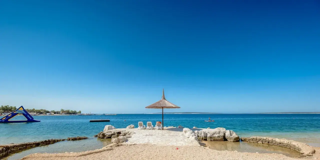 Słoneczny dzień na plaży w Simuni camping. Leżaki pod parasolem, dmuchany plac zabaw w wodzie i błękitne morze.