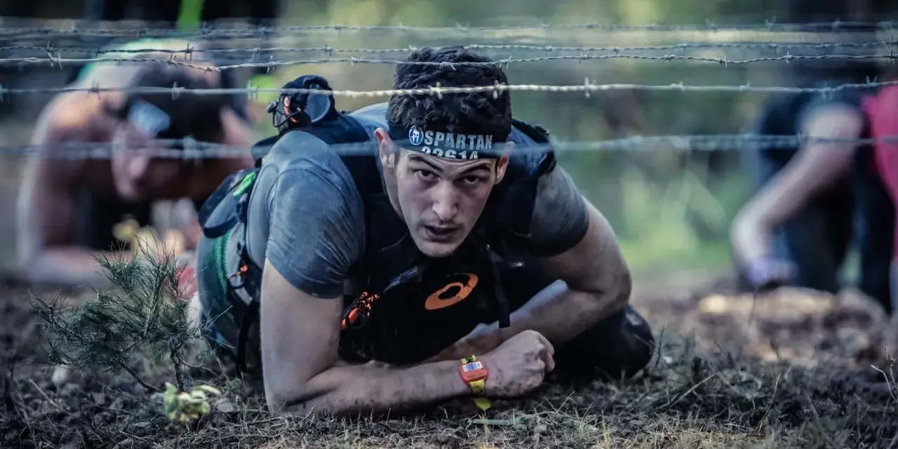 En man kryper under taggtråd under ett ocr sport-lopp.