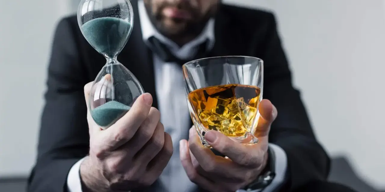 Mann im Anzug hält Sanduhr und Whiskyglas. Die Frage, ob kann Whisky schlecht werden, wird durch die vergehende Zeit und den edlen Tropfen symbolisiert.