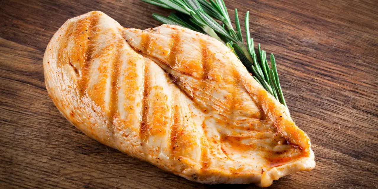 Grillowana pierś z kurczaka z rozmarynem na drewnianej desce. Zastanawiasz się, ile białka ma pierś z kurczaka? To świetne źródło!
