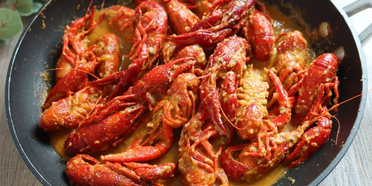 Un delicioso cangrejo de río en una sartén, bañado en una cremosa salsa. ¡Un manjar listo para disfrutar!