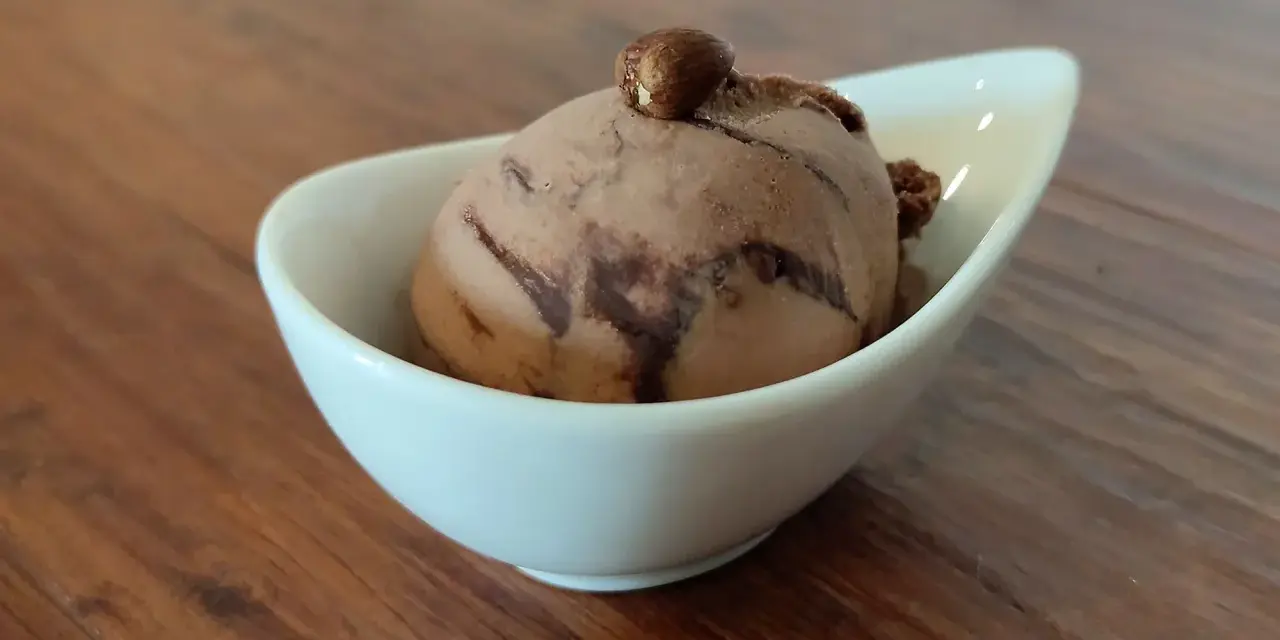 Ein Bacio Eis in einer weißen Schale, gekrönt von einer Haselnuss. Ein süßer Genuss auf Holztisch.