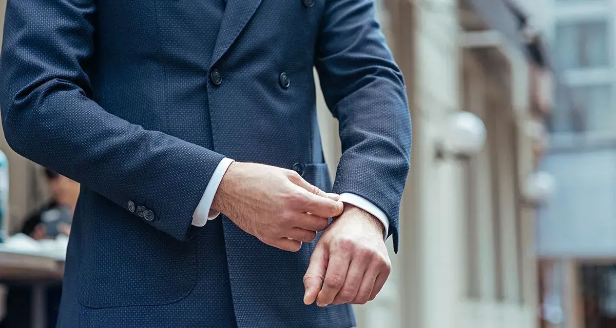 Uomo che sistema il polsino della sua giacca blu, un perfetto abbinamento giacca blu uomo per un look elegante.