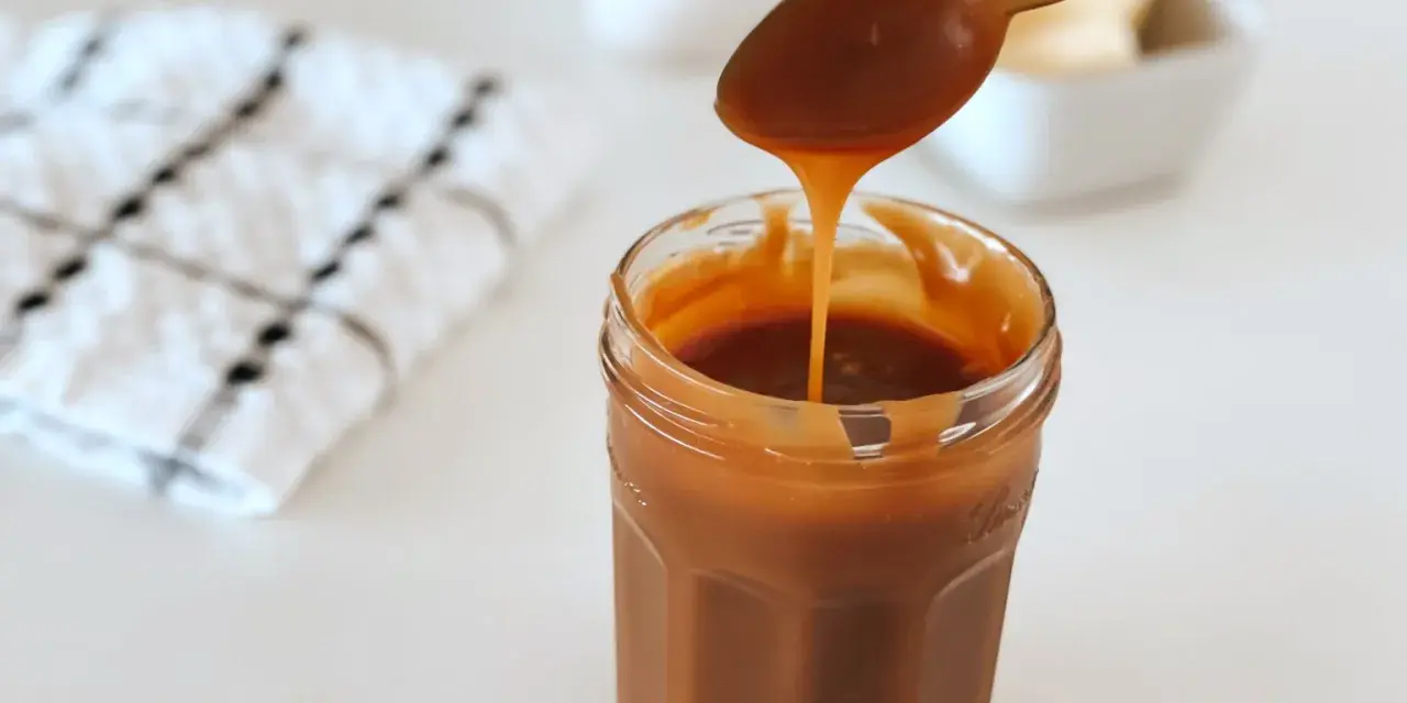 Une cuillère verse du caramel onctueux dans un pot. La recette caramel parfaite pour vos desserts.