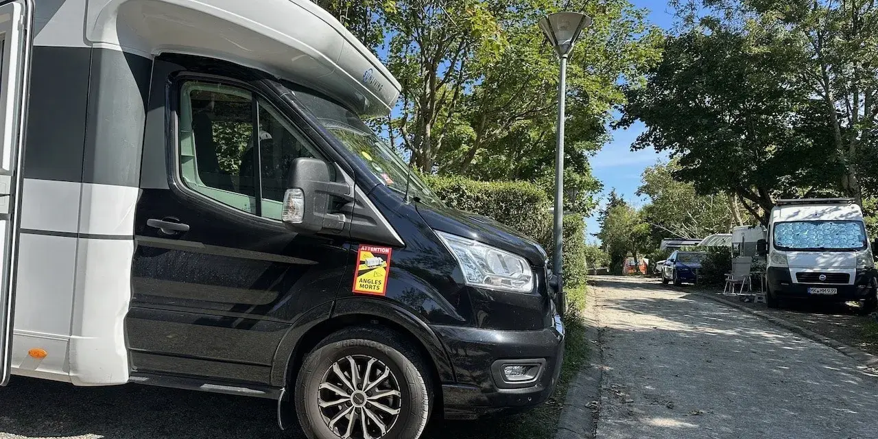 Husbil parkerad på en campingplats vid frankrike kust. Soligt väder med träd och andra husbilar i bakgrunden.