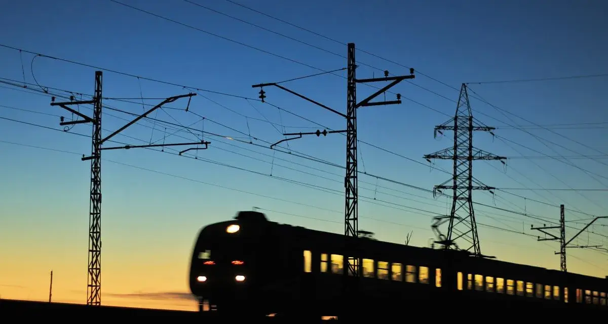 Pociąg w ruchu na tle zachodzącego słońca i linii energetycznych.