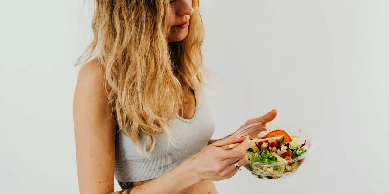 Donna con capelli biondi mangia un'insalata fresca, parte della sua vlckd dieta.