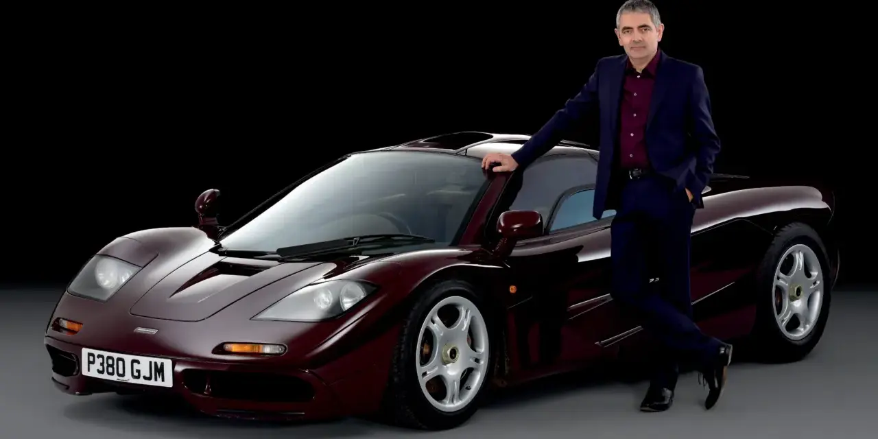 Rowan Atkinson w garniturze opiera się o swój bordowy McLaren F1. To jeden z jego ulubionych samochodów.