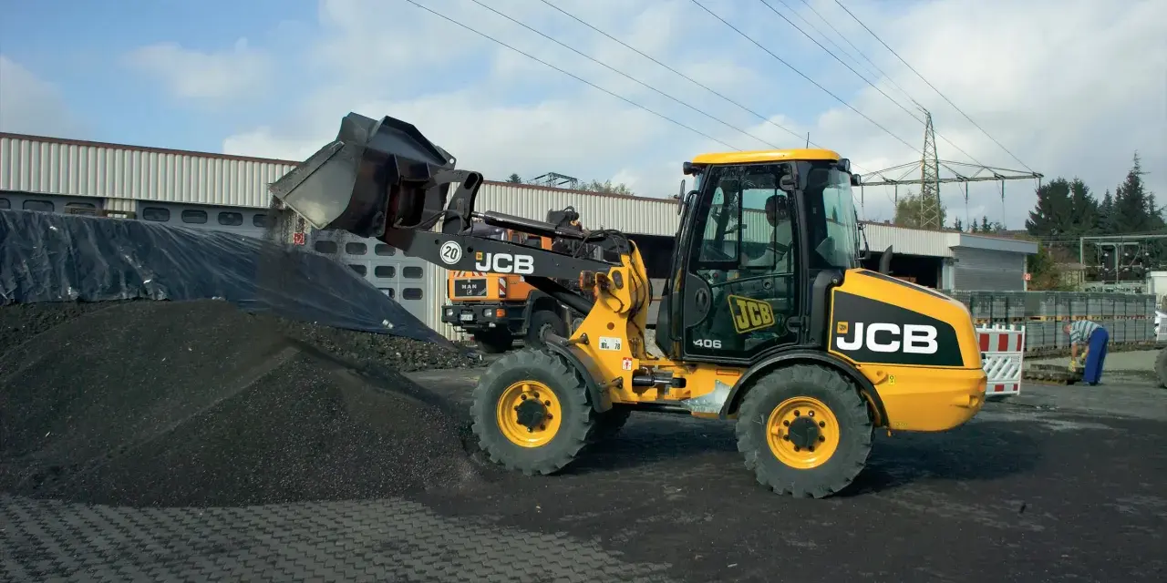 Żółta ładowarka JCB 406 z podniesioną łyżką, gotowa do pracy. Dane techniczne tej maszyny pozwalają na efektywne przenoszenie materiałów.