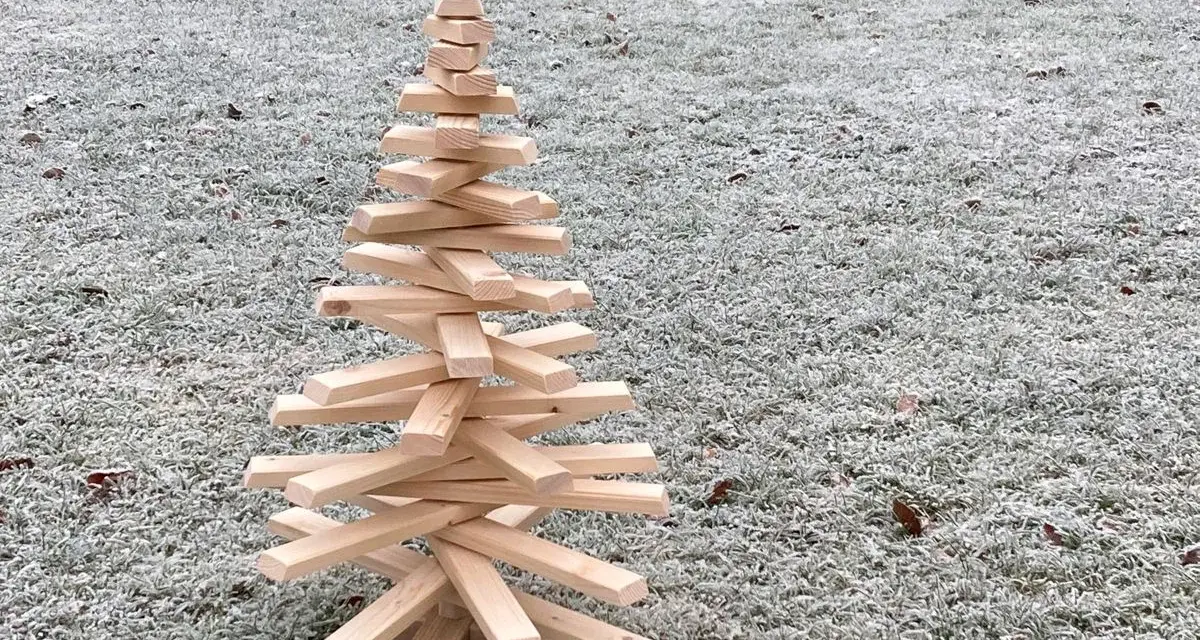 Ein selbstgemachter Tannenbaum aus Holz, der auf frostigem Gras steht. Eine rustikale Deko-Idee, um den Winter zu begrüßen.