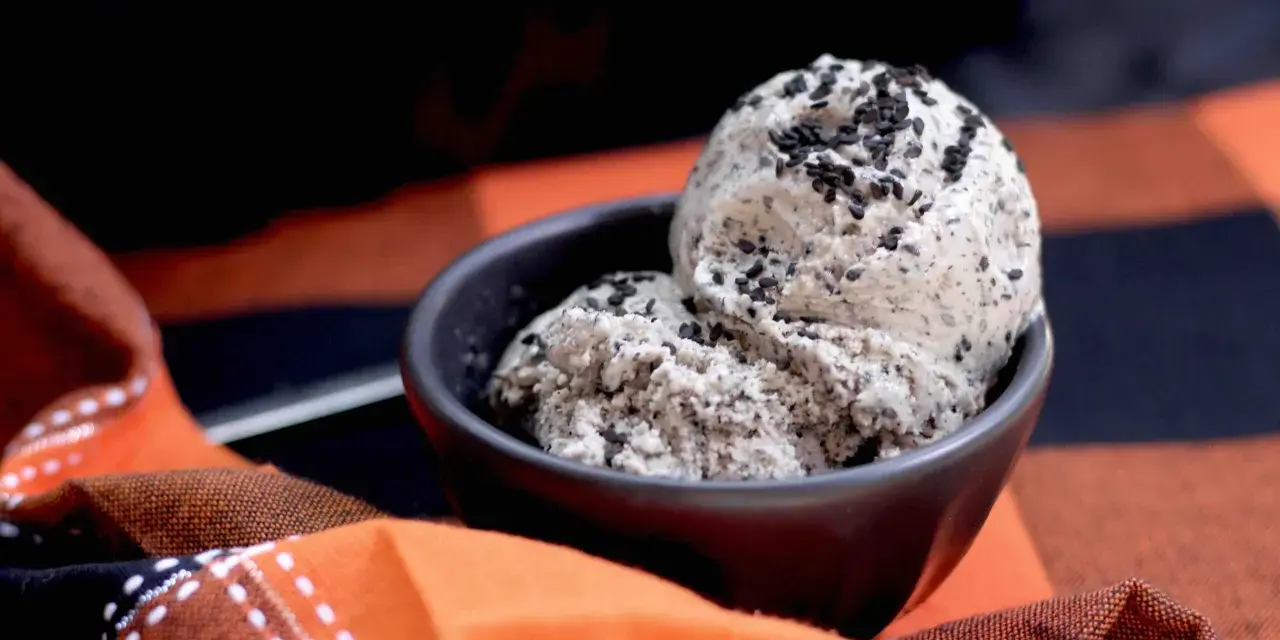 Zwei Kugeln cremiges **black sesame ice cream** in einer Schale, bestreut mit schwarzen Sesamsamen, auf einem karierten Stoff.