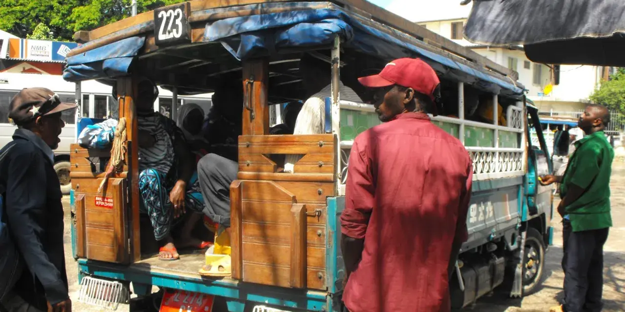 Ludzie wsiadają do dala dala na Zanzibarze. Widać drewnianą konstrukcję pojazdu i pasażerów.