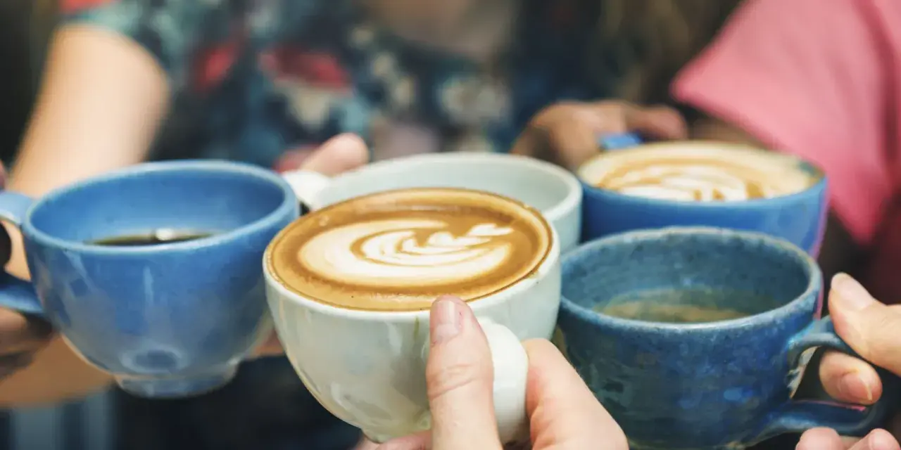 Vier Hände halten bunte Kaffeetassen. Der Kaffee reizt die Blase, aber der Genuss ist es wert.