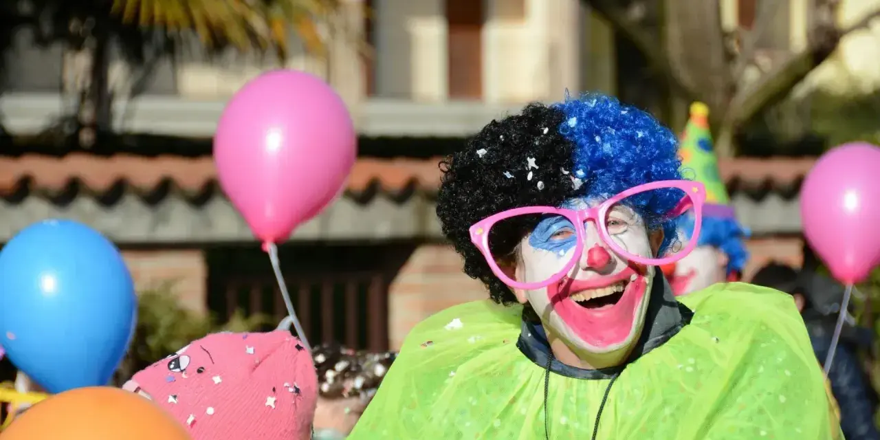 Uśmiechnięty animator w peruce i okularach, otoczony balonami, przygotowuje się do zabawy.