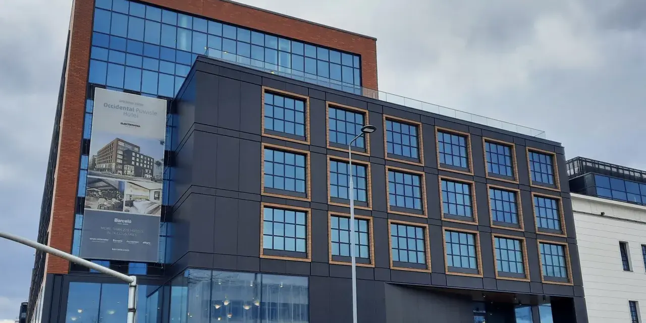 Nowoczesny budynek z cegły i ciemnej fasady, z banerem zapowiadającym otwarcie Occidental Powisle Hotel, części sieci Barceló.