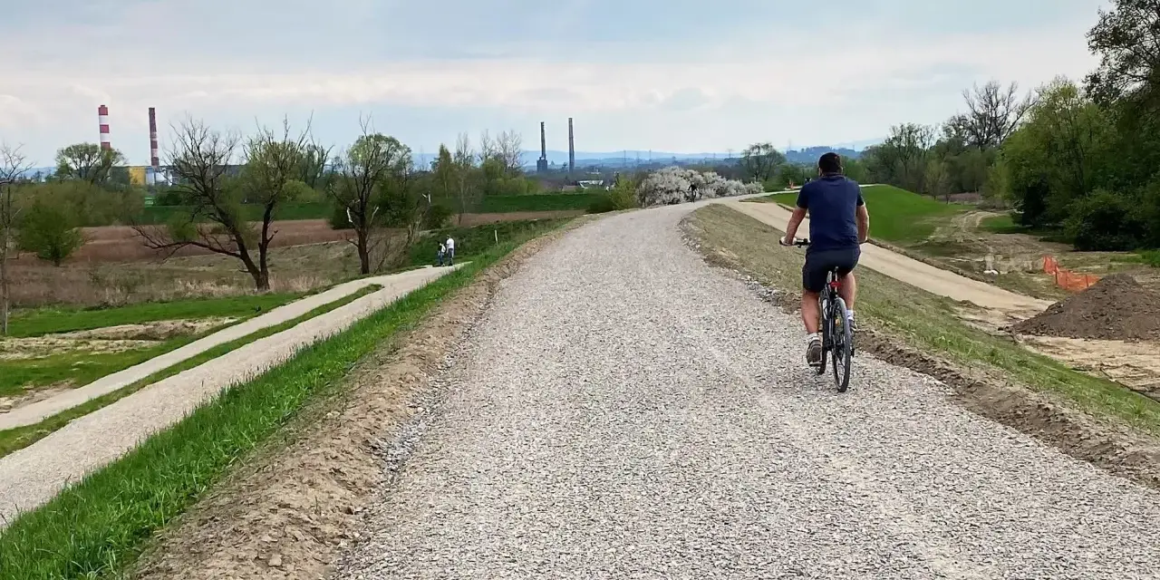Mężczyzna na rowerze przemierza nową ścieżkę rowerową w Skawinie. W tle widać przemysłowe kominy i zielone tereny.