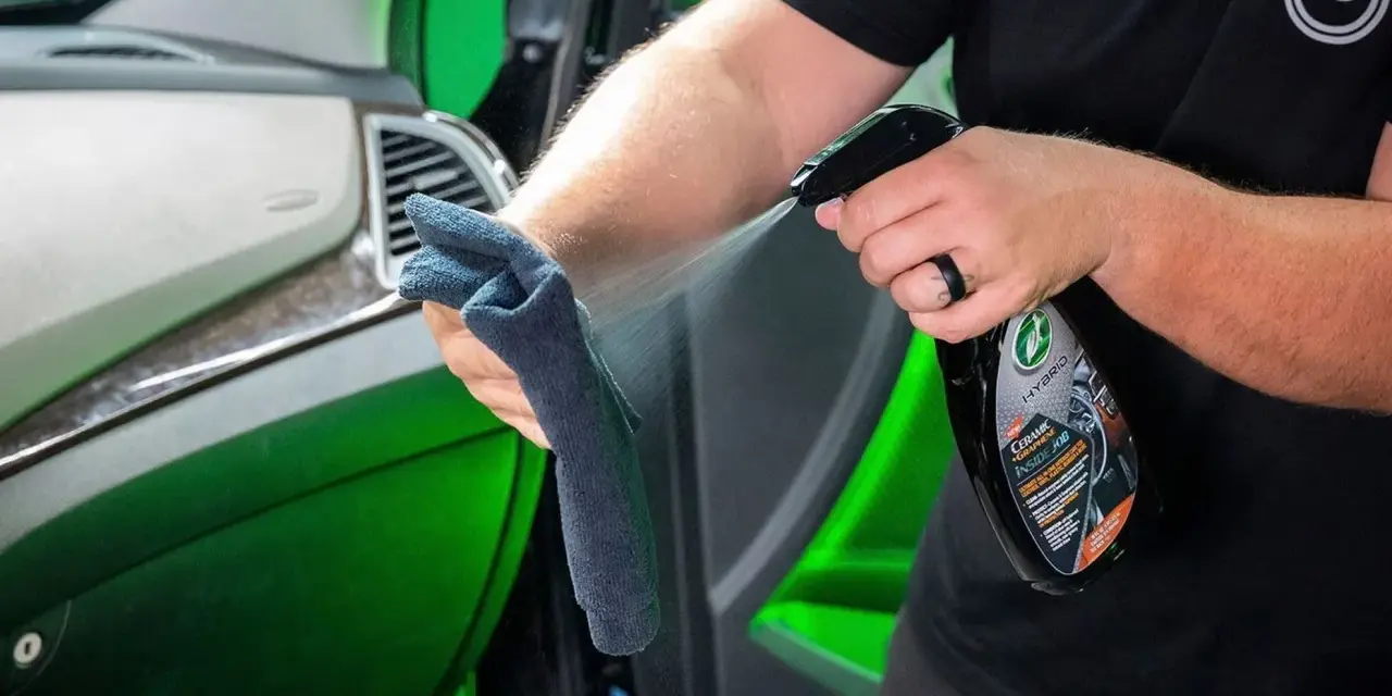 Person sprayar en trasa med en produkt för bilvård, en effektiv wax remover, för att rengöra bilens interiör.