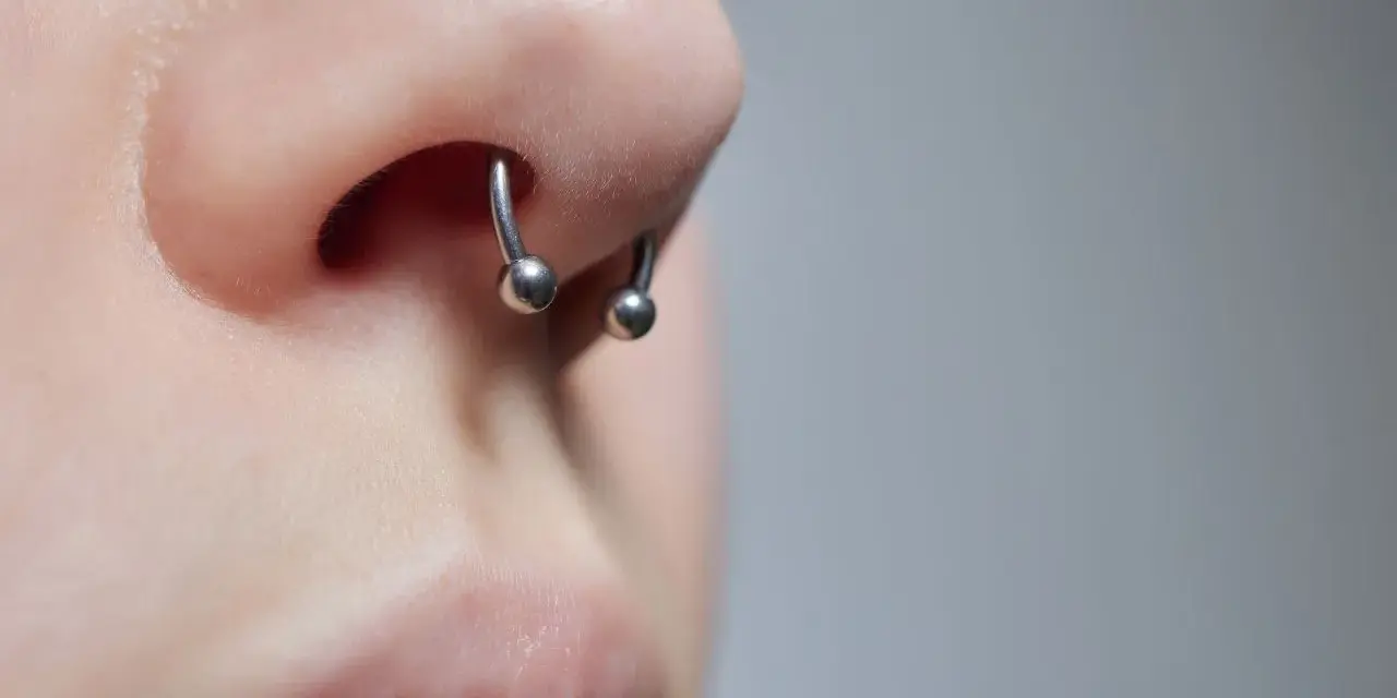 Zbliżenie na nos z kolczykiem typu septril piercing. Metalowy okrąg z dwoma kulkami subtelnie zdobi przegrodę nosową.