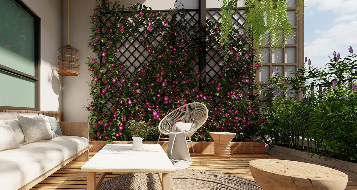 Un terrazzo fiorito con rampicanti rosa su una grata, un divano bianco, tavolino e seduta in rattan. Un'idea per come abbellire una parete con la natura.
