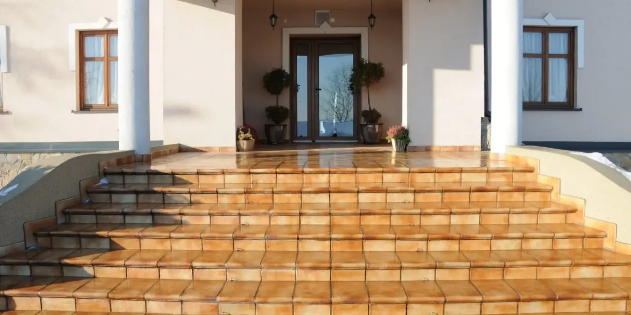 Amplias escaleras exteriores para casas de dos pisos, con escalones de baldosas naranjas que conducen a una entrada principal.