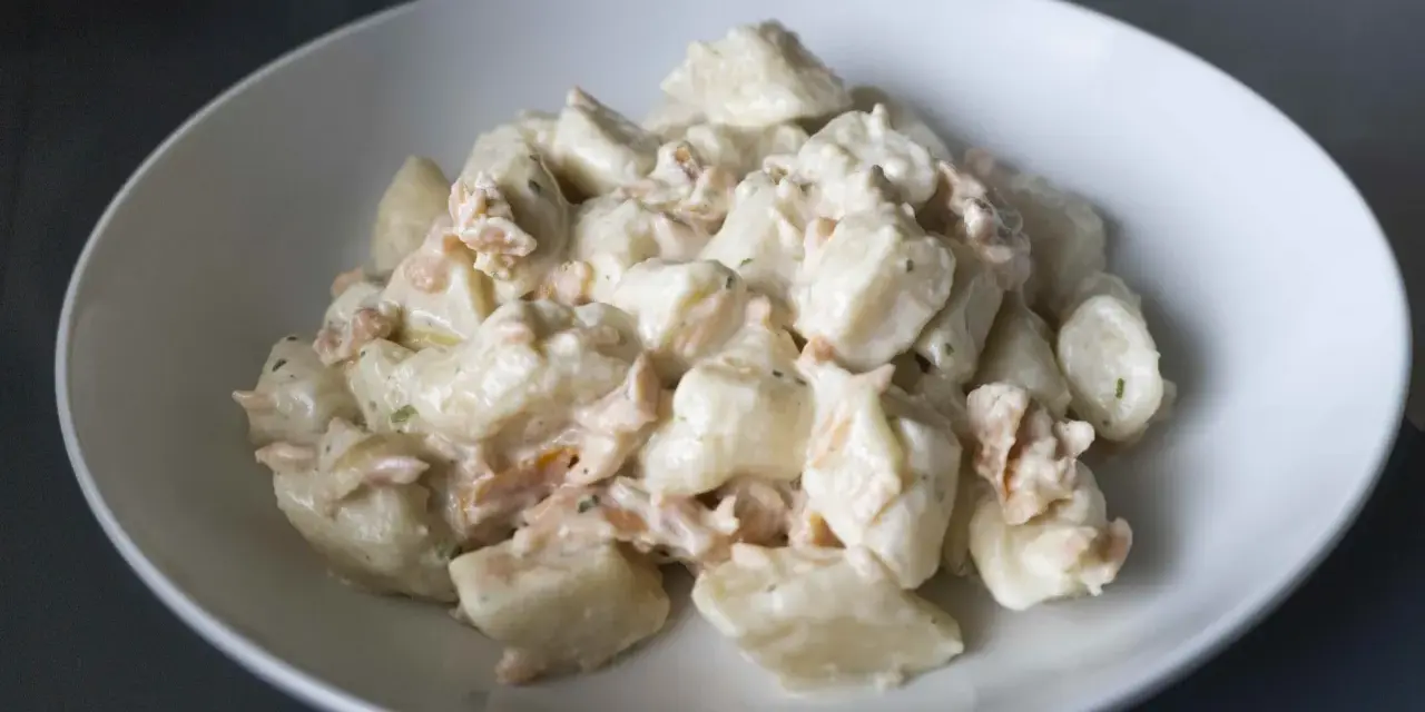 Gnocchi ziemniaczane kontra gnocchi z ricotty w kremowym sosie z łososiem. Pyszne danie w białej misce.
