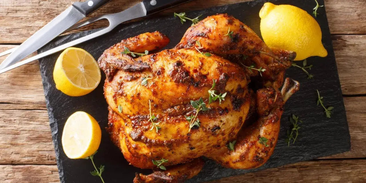 Pollo al horno dorado y jugoso, adornado con tomillo fresco y acompañado de limones cortados. Un festín listo para servir.