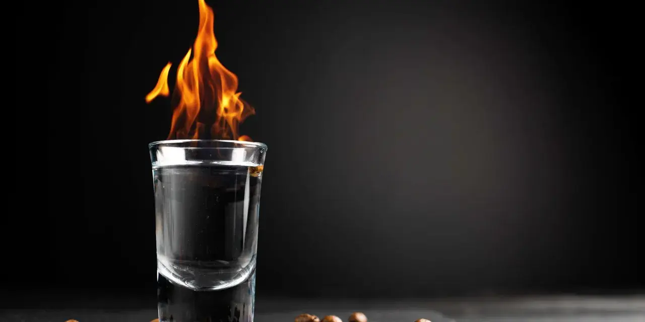 Ein Schnapsglas mit brennendem Sambuca und Kaffeebohnen. Die Flammen tanzen, ein Spektakel, das erklärt, warum brennt Sambuca.