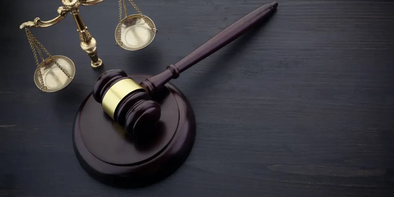 Wniosek o zamianę prac społecznych na potrącenie z wynagrodzenia wzór. Młotek sędziowski i waga sprawiedliwości na ciemnym tle.