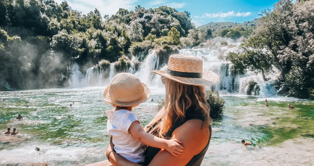 Mama z dzieckiem podziwia wodospady w parku Krka w Chorwacji. Woda jest krystalicznie czysta, a wokół bujna zieleń.