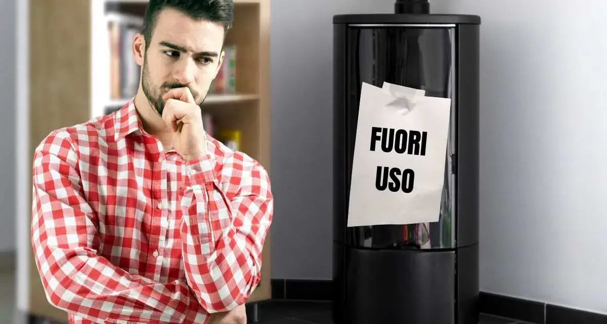 Uomo pensieroso guarda stufa spenta con foglio "FUORI USO". Necessaria riparazione stufe per il freddo.
