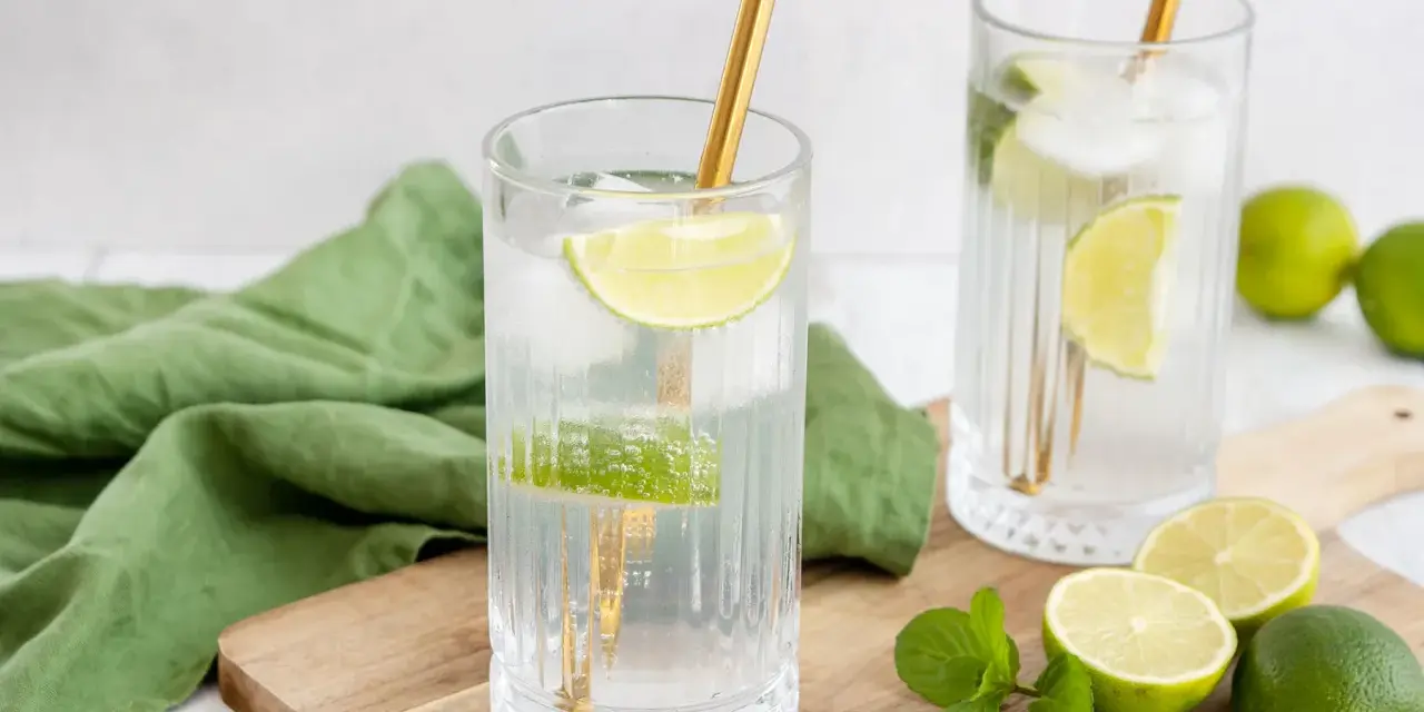 Erfrischende Drinks: Zwei Gläser mit Eis, Limettenscheiben und goldenen Strohhalmen. Perfekt zum **Wodka mischen** an einem warmen Tag.