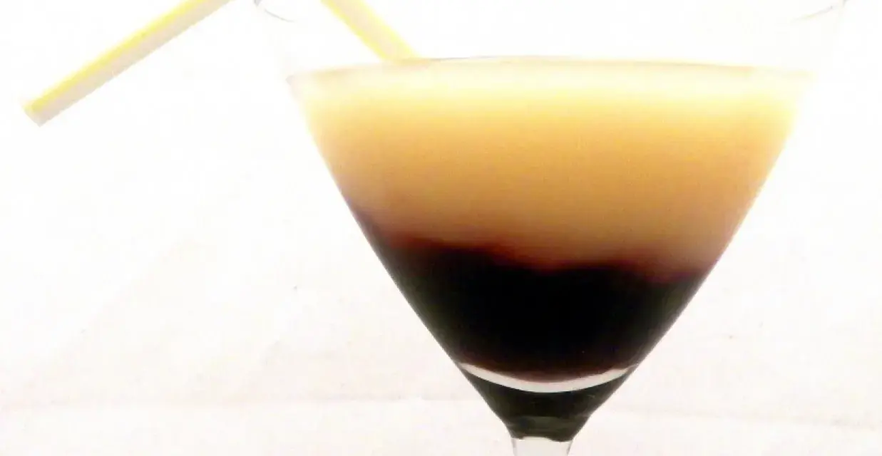 Dwukolorowy drink w kieliszku, z warstwą soku z czarnej porzeczki na dnie i jasnym płynem na górze, ozdobiony żółtą słomką.