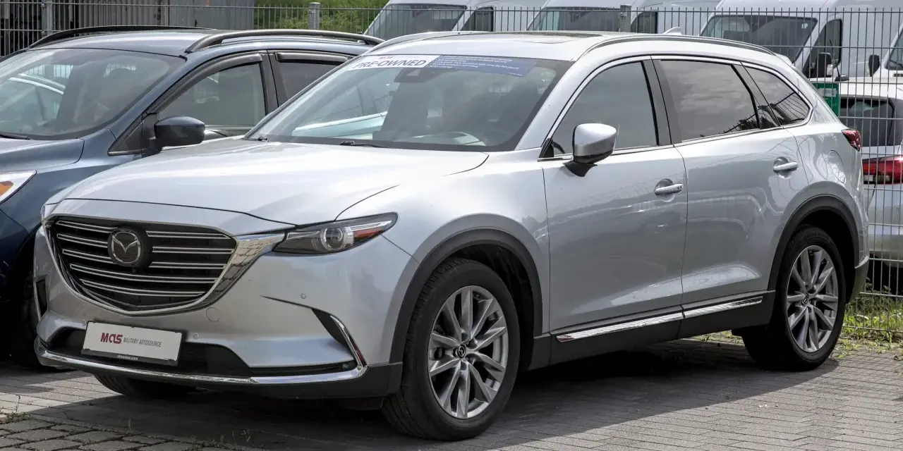 Srebrna Mazda CX-9 z napisem "PRE-OWNED" na przedniej szybie, zaparkowana na zewnątrz.
