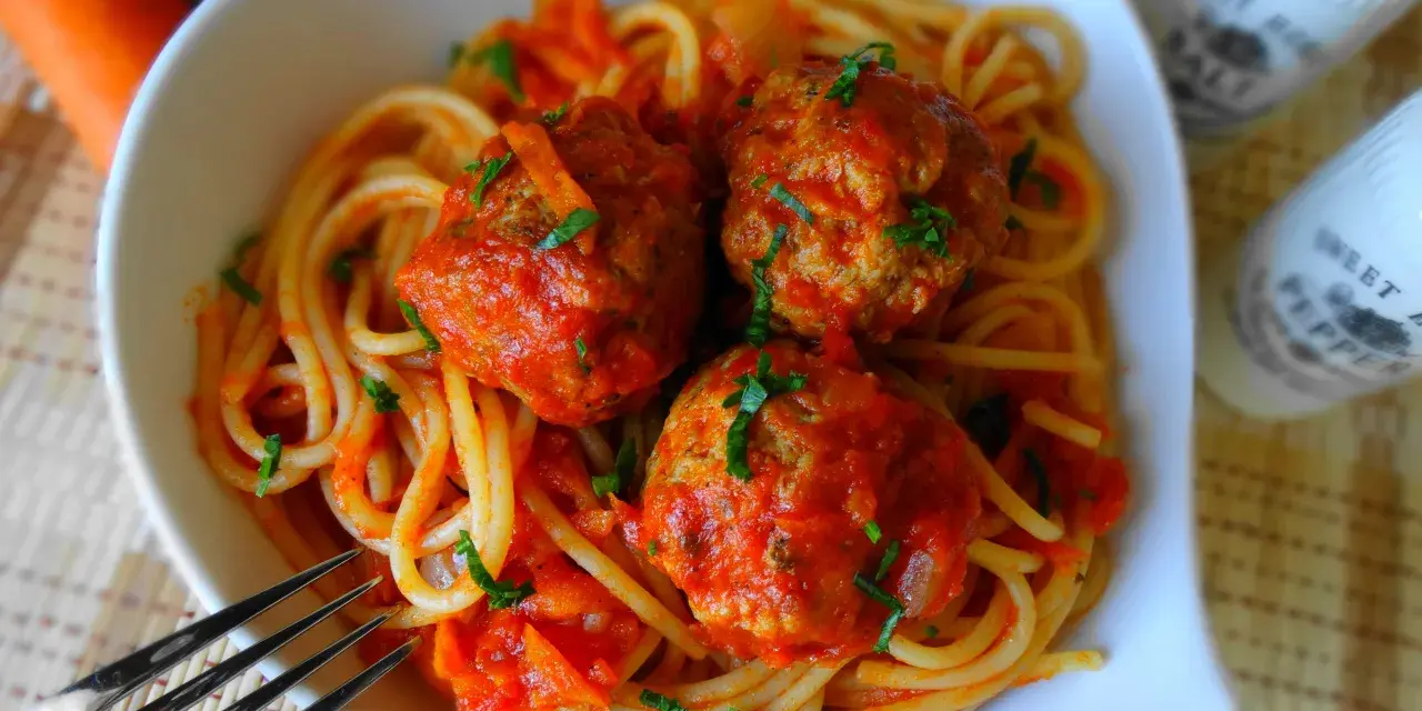Pyszne spaghetti z klopsikami w sosie pomidorowym, posypane natką pietruszki. Idealne danie dla całej rodziny.