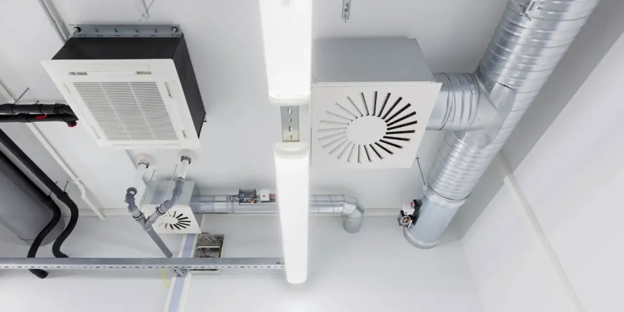 Detalles de sistemas de ventilación y extracción de aire, incluyendo conductos metálicos, unidades de aire acondicionado y luces fluorescentes en un techo.