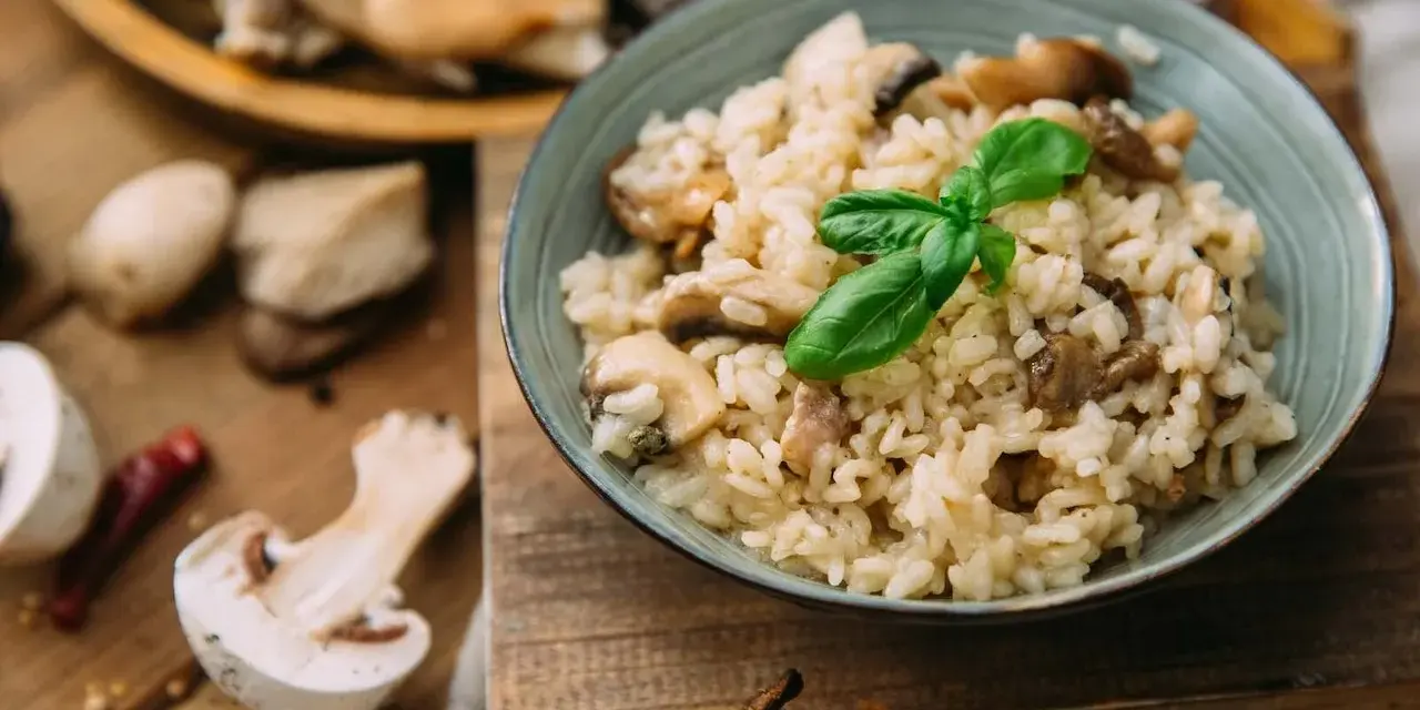 Miseczka kremowego risotto z grzybami i bazylią, otoczona świeżymi grzybami i przyprawami.