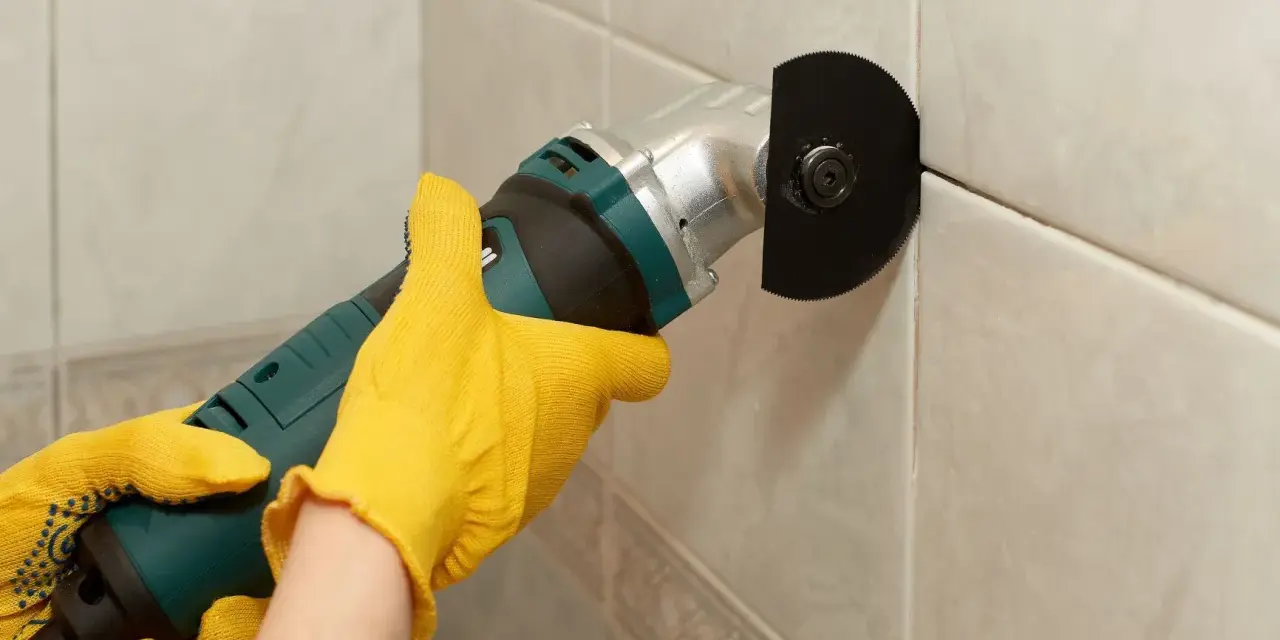 Mit gelben Handschuhen wird eine Fugenfräse benutzt, um Fliesen zu reparieren.