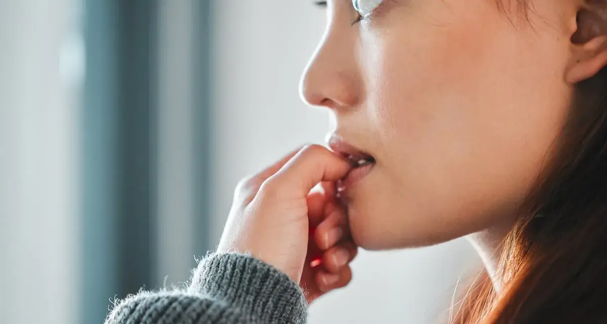 Une jeune femme songeuse, les doigts près de la bouche, réfléchit à comment arrêter de se ronger les ongles.